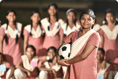 A schoolgirl holding a football, with her teammates seated behind her